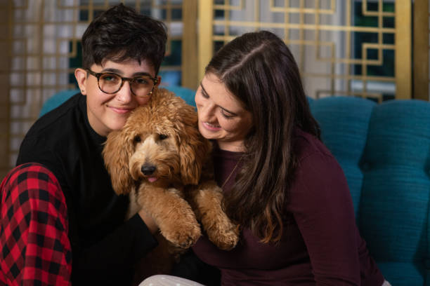 Two lesbian women lounging on the couch holding their new golden doodle puppy.