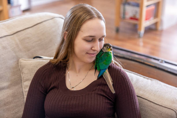 Portrait of a young woman at home with her green-cheek Conure named Momo.