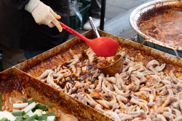 Stir-fried chicken feet for sale at a traditional market in Korea and a merchant's hand cooking with a ladle